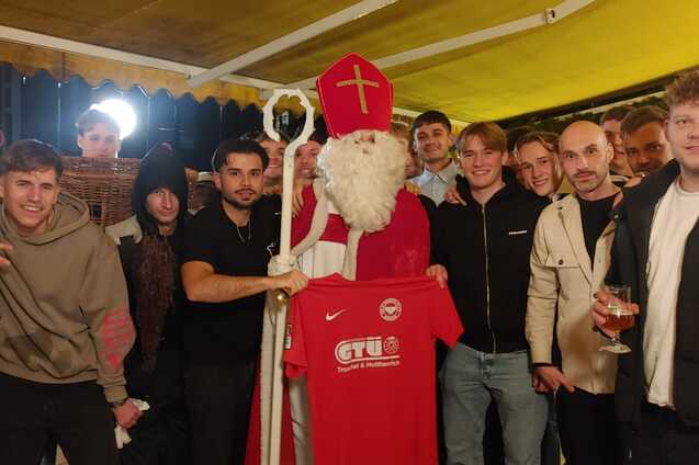 Gruppe junger Menschen posiert mit einem Santa Claus, der ein rotes T-Shirt h&auml;lt, in einer festlich dekorierten Umgebung.