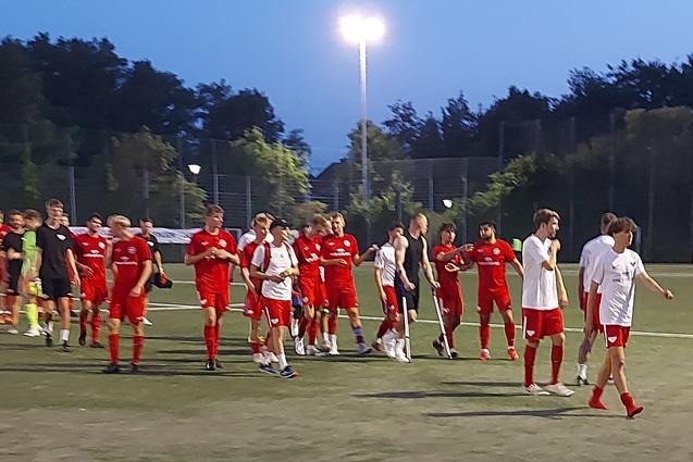 Gruppe von Fu&szlig;ballspielern in roten und blauen Trikots auf einem Kunstrasenplatz bei D&auml;mmerung.
