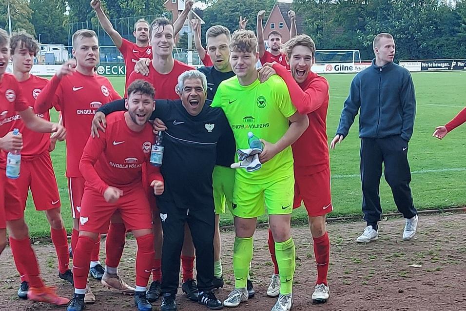 Gruppe jubelnder Fu&szlig;ballspieler in roten Trikots, umrahmt von einem Torwart in gr&uuml;ner Ausr&uuml;stung auf dem Spielfeld.
