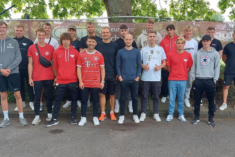 Gruppe von 20 jungen M&auml;nnern in Trainingsanz&uuml;gen steht auf einem Platz vor einem Zaun mit Werbebanner.
