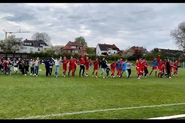 Gruppierung von Spielern und Fans, die gemeinsam auf einem Fu&szlig;ballplatz jubeln und tanzen, umgeben von Wohnh&auml;usern.