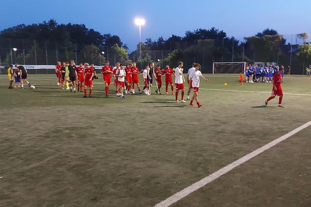 Gruppe von Fu&szlig;ballspielern in roten und blauen Trikots auf einem Kunstrasenplatz bei D&auml;mmerung.