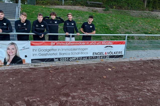Sechs Personen in schwarzer Kleidung stehen l&auml;chelnd vor einem Banner der Immobilienagentur Engel & V&ouml;lkers.