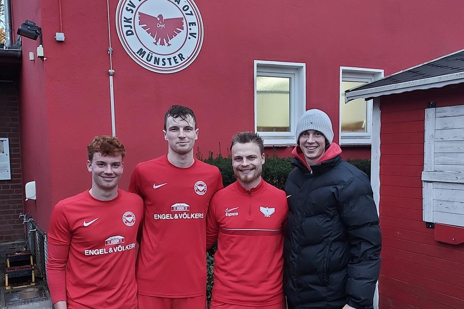 Vier Personen in roten Fu&szlig;balltrikots stehen vor einem Geb&auml;ude mit Vereinslogo und einem wei&szlig;en Nebenbau.