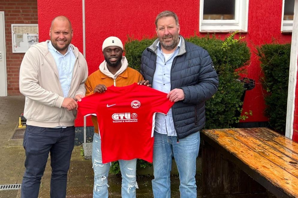 Drei M&auml;nner stehen vor einem Vereinsgeb&auml;ude und halten ein rotes Trikot des Fu&szlig;ballvereins Borussia M&uuml;nster.