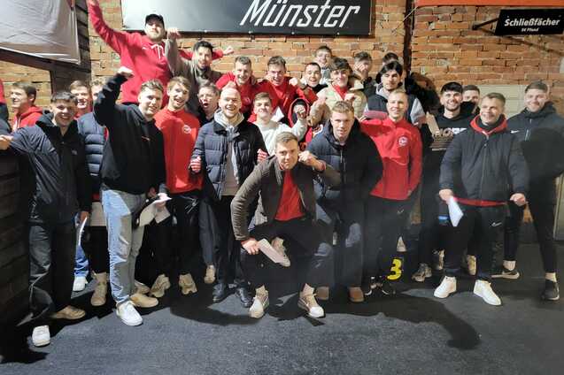 Gruppennfoto einer Fu&szlig;ballmannschaft in roten Trikots, l&auml;chelnd und posierend in einer Indoor-Location.