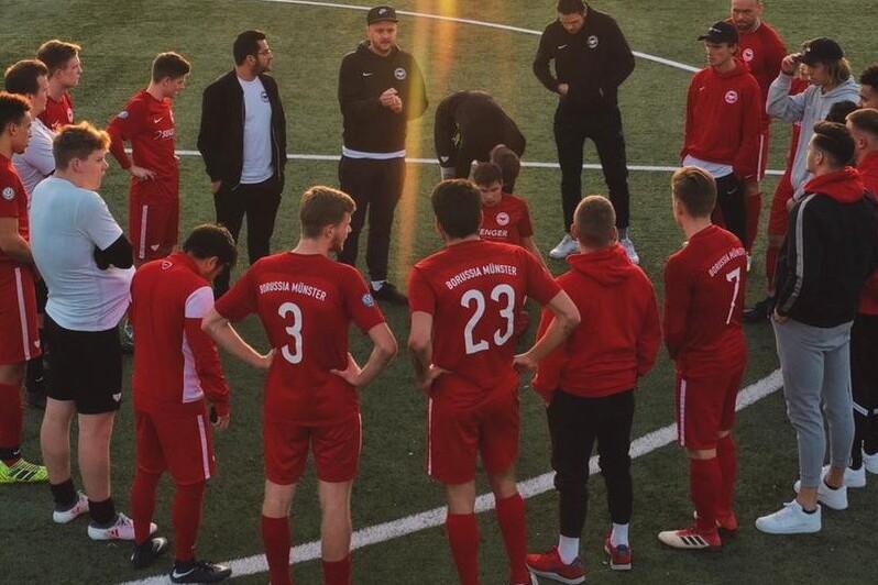 Gruppe von Fu&szlig;ballspielern in roten Trikots versammelt sich auf dem Rasen zur Besprechung.