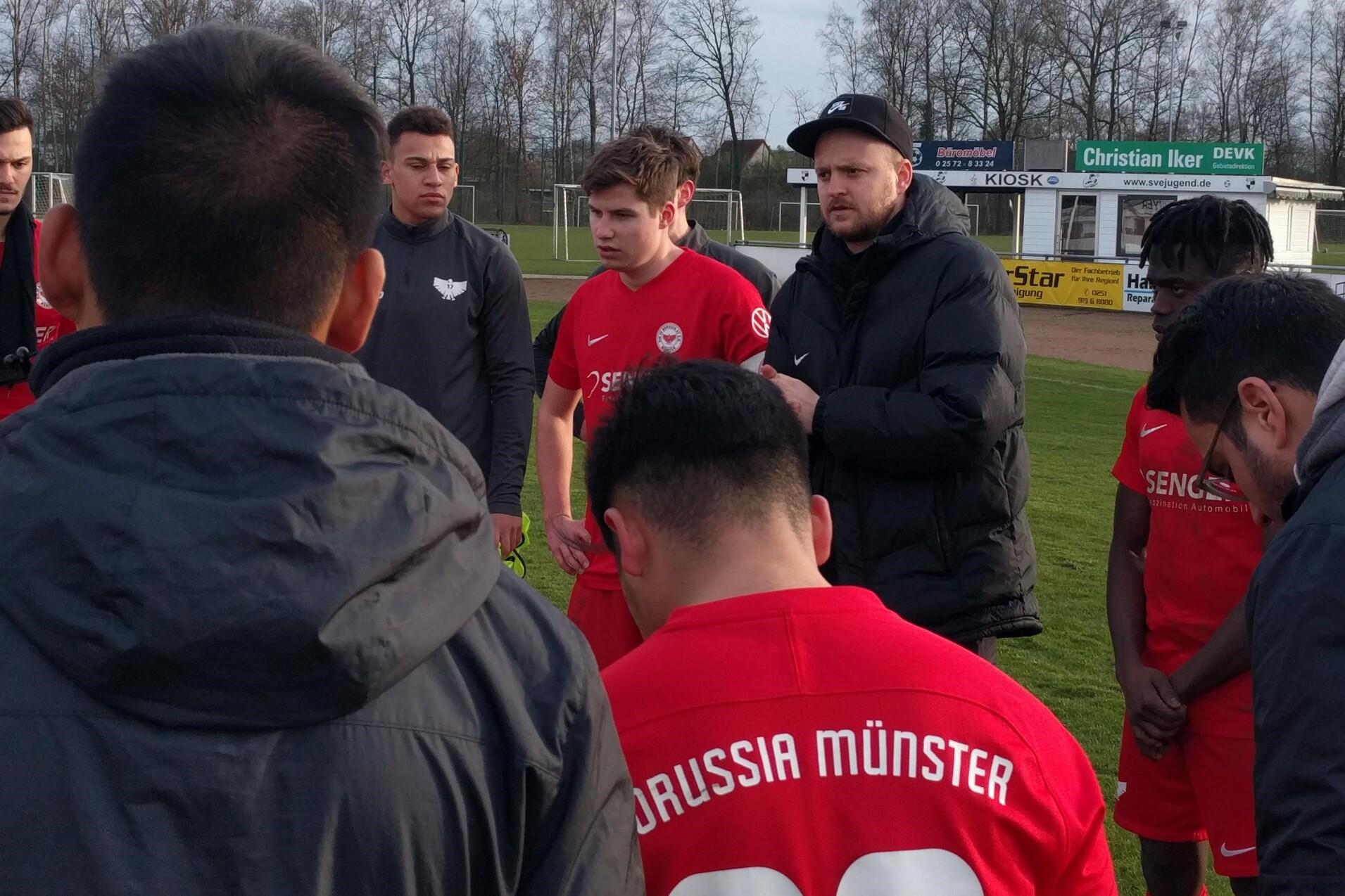 Gruppenbesprechung von Fu&szlig;ballspielern in roten Trikots auf dem Platz, Coach gibt Anweisungen.