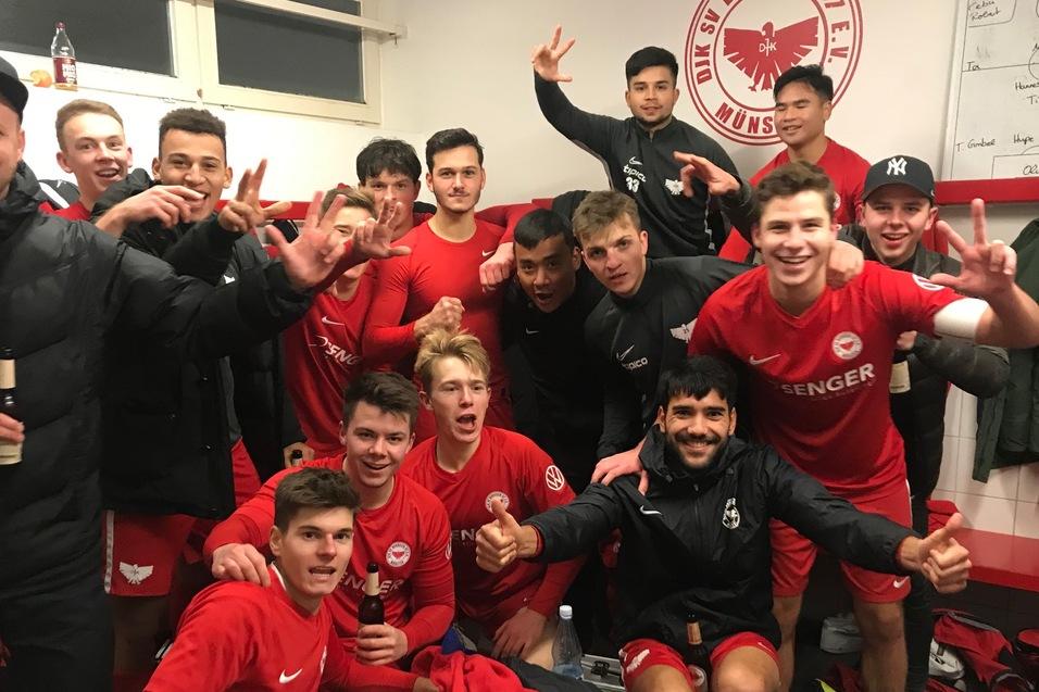 Gruppe junger Fu&szlig;ballspieler in roten Trikots posieren fr&ouml;hlich in einer Umkleidekabine nach einem Sieg.