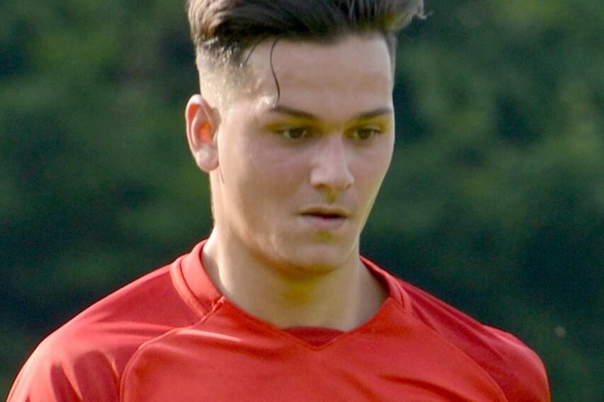 Ein junger Fu&szlig;ballspieler in rotem Trikot steht auf dem Platz mit determinierter Miene.