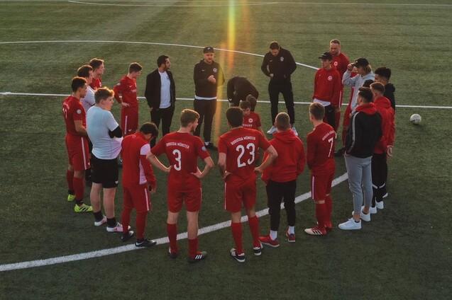 Gruppe von Fu&szlig;ballspielern in roten Trikots versammelt sich auf dem Rasen zur Besprechung.