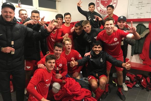 Gruppe junger Fu&szlig;ballspieler in roten Trikots posieren fr&ouml;hlich in einer Umkleidekabine nach einem Sieg.