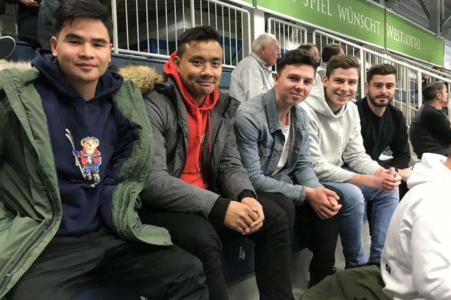 F&uuml;nf junge M&auml;nner sitzen nebeneinander in einer Trib&uuml;ne, jeder in unterschiedlichen Freizeitoutfits.