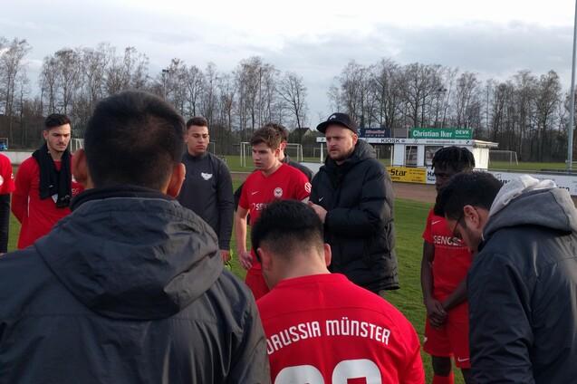 Gruppenbesprechung von Fu&szlig;ballspielern in roten Trikots auf dem Platz, Coach gibt Anweisungen.
