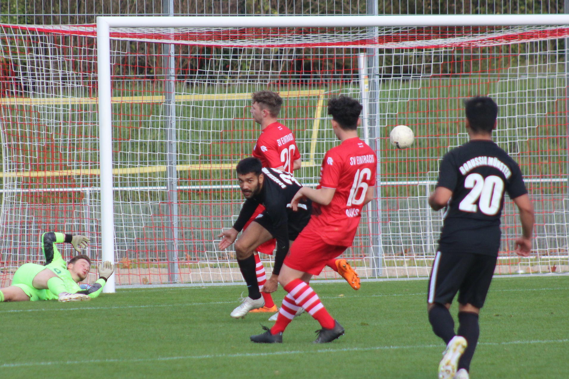 Fu&szlig;ballspiel: Spieler in roten Trikots schie&szlig;en auf das Tor, Torwart springt, um den Ball zu halten.