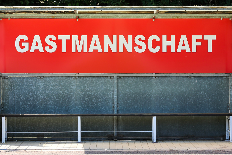 Sitzbank f&uuml;r die Gastmannschaft mit rotem Schild auf einem Sportplatz.