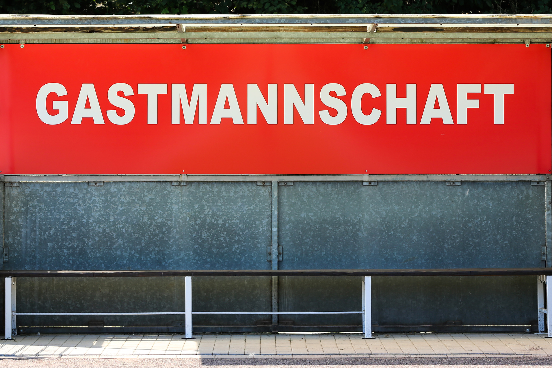Sitzbank f&uuml;r die Gastmannschaft mit rotem Schild auf einem Sportplatz.