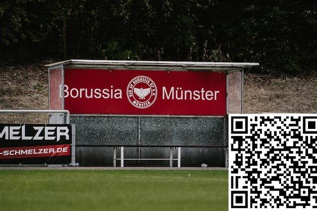 Sitzbank mit dem Logo von Borussia M&uuml;nster und einem QR-Code auf einem Fu&szlig;ballfeld.