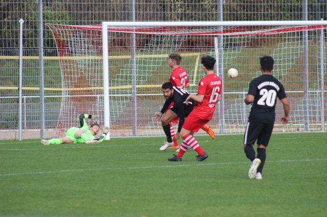 Fu&szlig;ballspiel: Spieler in roten Trikots schie&szlig;en auf das Tor, Torwart springt, um den Ball zu halten.