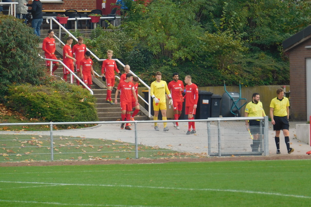 Fu&szlig;ballmannschaft in roten Trikots betritt das Spielfeld, gefolgt von Schiedsrichtern in gelben Trikots.