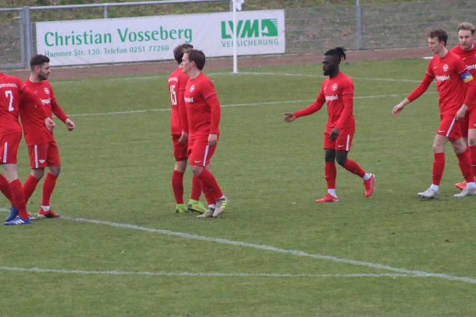 Fu&szlig;ballmannschaft in roten Trikots jubelt auf dem Spielfeld nach einem Erfolg, Hintergrund mit Werbebannern.