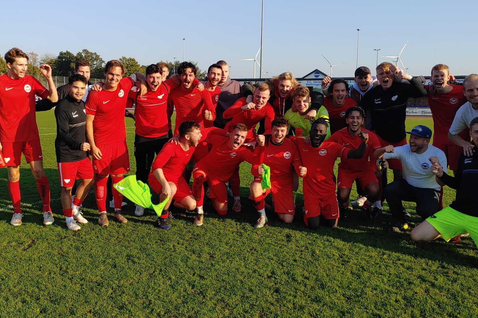 Gruppennaufnahme einer Fu&szlig;ballmannschaft in roten Trikots, die auf einem Rasenfeld steht und jubelt.