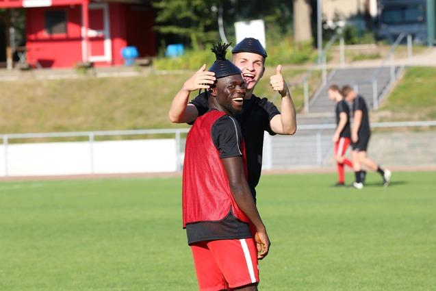 Zwei Fu&szlig;ballspieler auf dem Trainingsplatz, ein Spieler tr&auml;gt ein rotes Shirt und lacht, der andere macht ein Daumen-hoch.