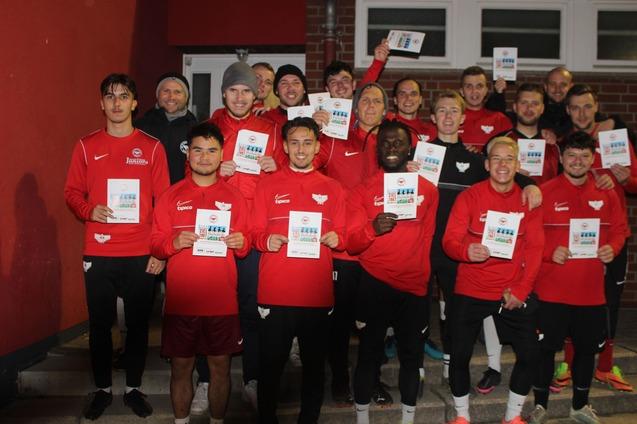 Gruppe von Fu&szlig;ballspielern in roten Trikots h&auml;lt Urkunden in der Hand, posierend vor einer roten Wand.