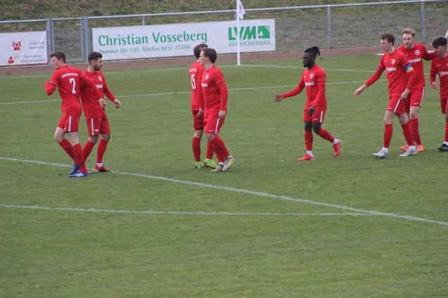 Fu&szlig;ballmannschaft in roten Trikots jubelt auf dem Spielfeld nach einem Erfolg, Hintergrund mit Werbebannern.