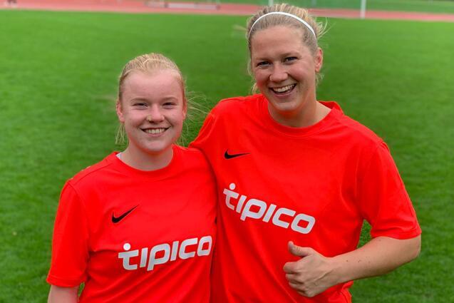 Zwei Fu&szlig;ballspielerinnen in roten Trikots mit "tipico"-Aufdruck l&auml;cheln auf einem Sportplatz.