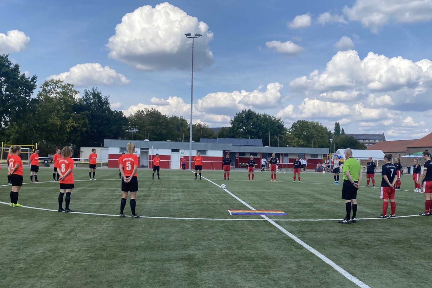 Zwei Fu&szlig;ballmannschaften stehen in einer Kreisformation auf dem Spielfeld, um einen Moment der Ehrung abzuhalten.