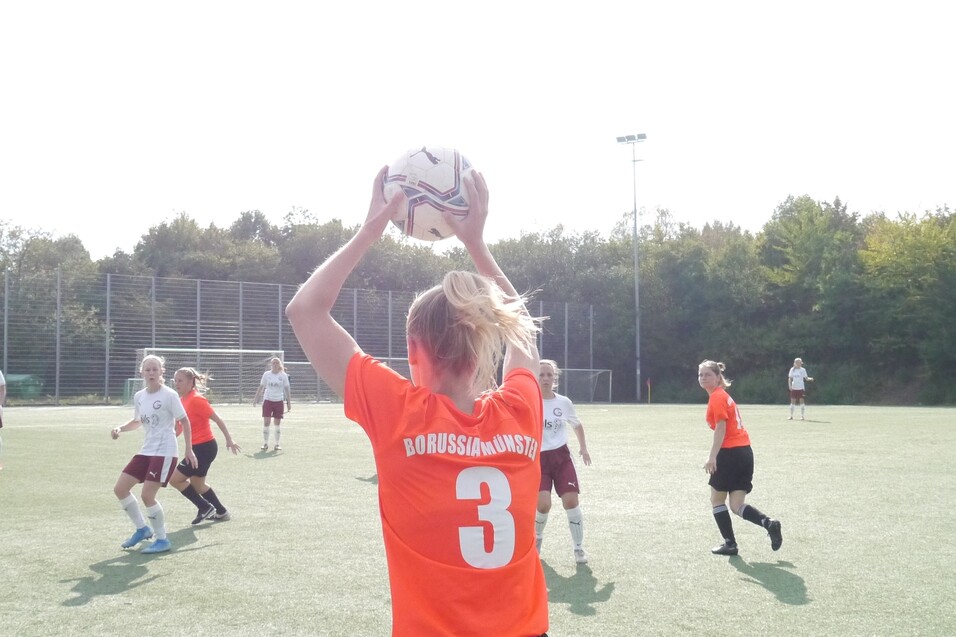 Spielerin in orange Trikot mit der Nummer 3 f&uuml;hrt einen Einwurf beim Fu&szlig;ballspiel auf einem Kunstrasenplatz aus.