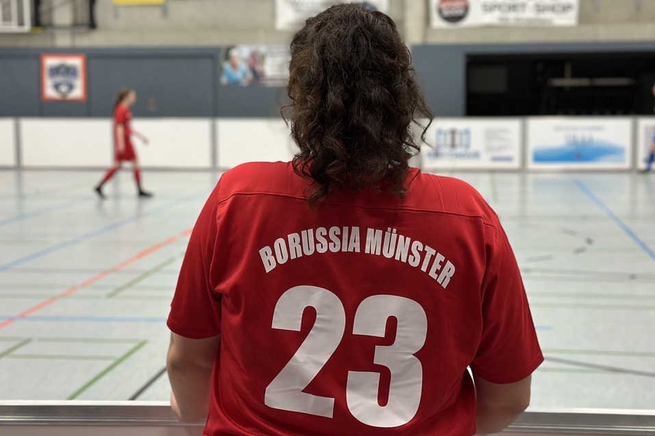 R&uuml;ckansicht einer Person in rotem Trikot mit &bdquo;Borussia M&uuml;nster&ldquo; und der Nummer 23, w&auml;hrend ein Hallenspiel stattfindet.