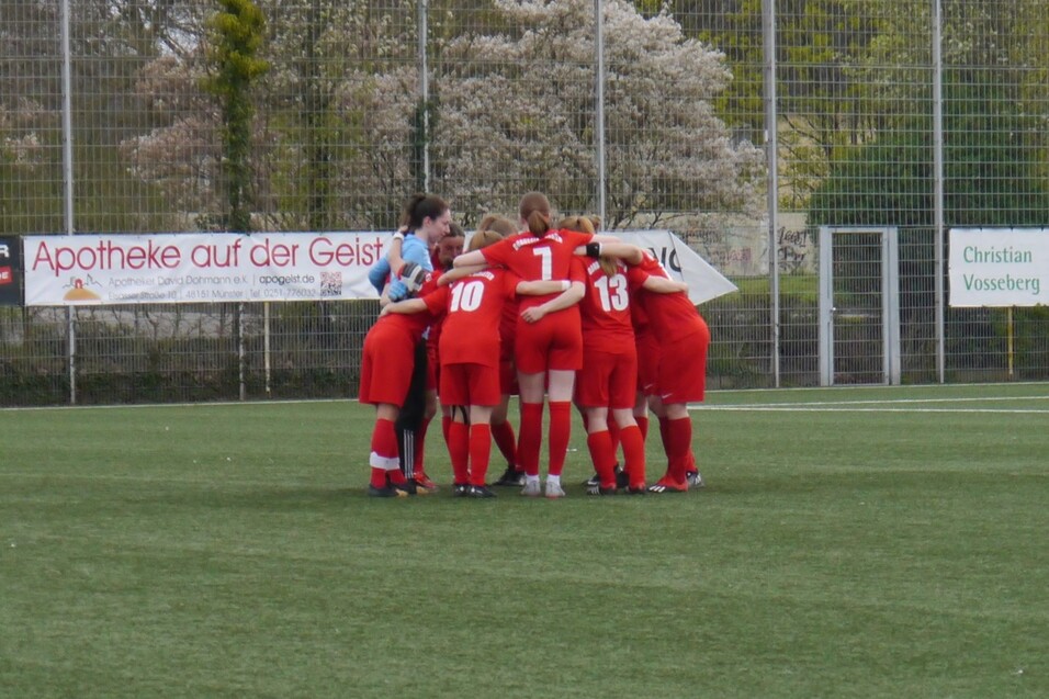 Eine Gruppe von Fu&szlig;ballspielerinnen in roten Trikots bildet einen Kreis auf dem Spielfeld.
