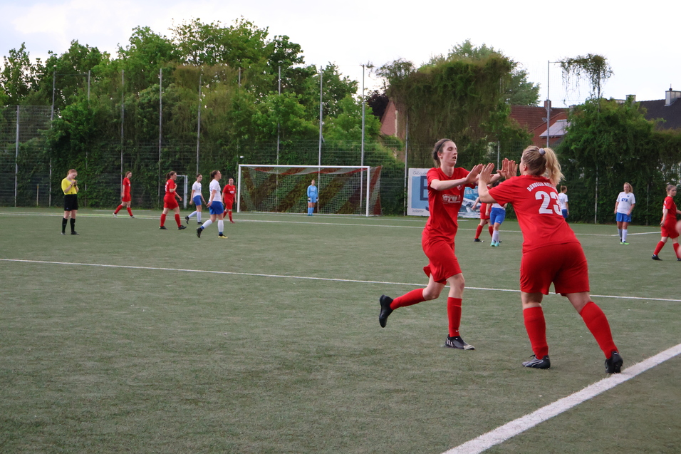 Zwei Spielerinnen in roten Trikots feiern auf einem Fu&szlig;ballfeld; im Hintergrund sichtbar Spielerinnen in blauen Trikots.