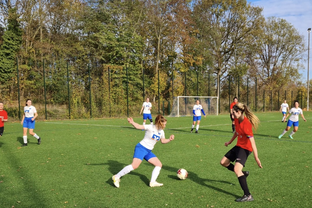 Zwei Spielerinnen stehen sich im Wettkampf auf einem Rasenplatz gegen&uuml;ber, w&auml;hrend andere Spielerinnen im Hintergrund agieren.