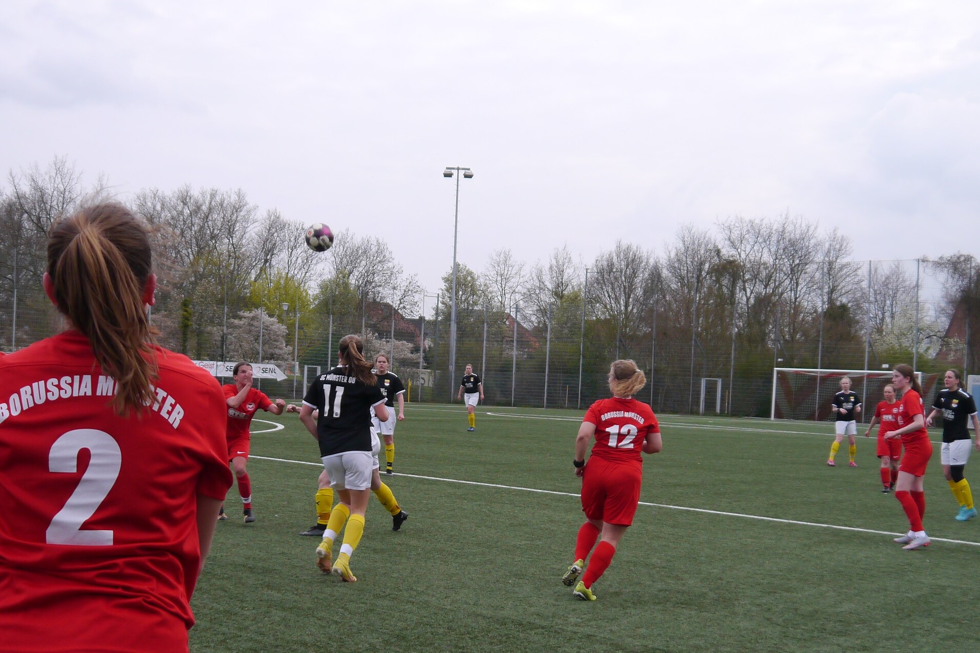 Frauenfu&szlig;ballspiel auf einem Kunstrasenplatz, Spielerinnen in roten und schwarzen Trikots zeigen eine Aktion mit Ball.