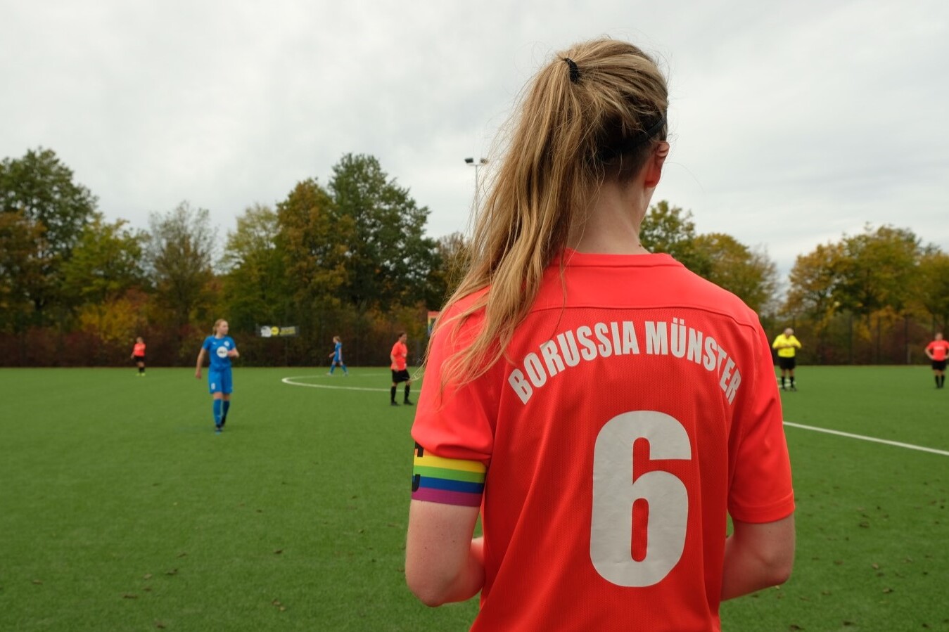 Frau mit langem Haar tr&auml;gt ein rotes Fu&szlig;balltrikot mit der Aufschrift "Borussia M&uuml;nster" und der Nummer 6.