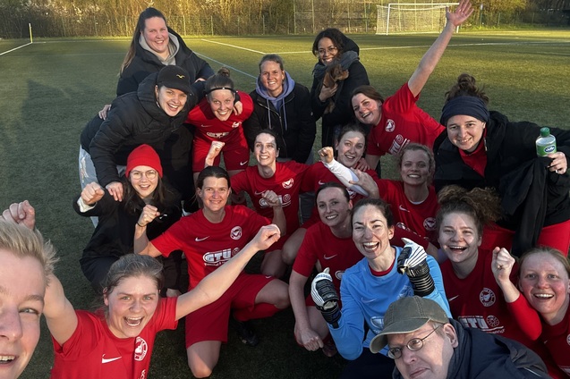 Gruppenselfie von Frauen in roten Fu&szlig;balltrikots auf einem Feld, alle l&auml;cheln und feiern gemeinsam.