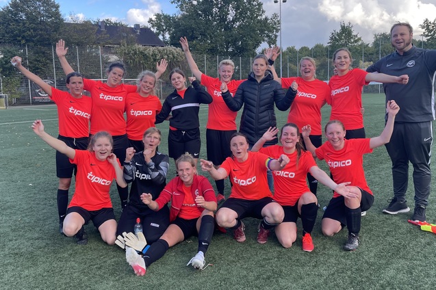 Gruppennahaufnahme eines Frauenfu&szlig;ballteams in roten Trikots, fr&ouml;hlich posierend auf dem Spielfeld.