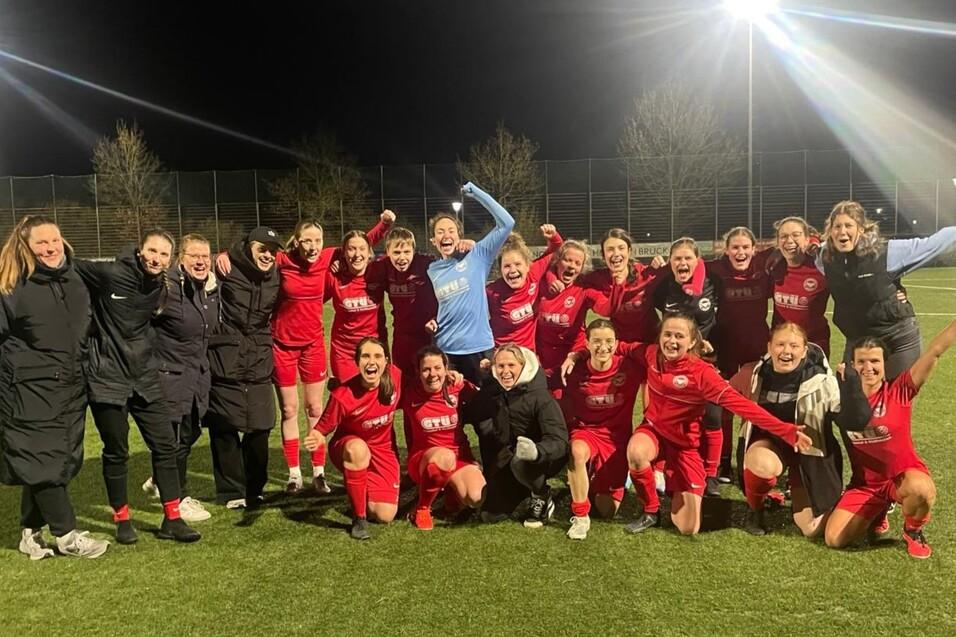 Gruppe von Frauenfu&szlig;ballspielerinnen in roten Trikots feiert nach einem Spiel auf dem Sportplatz bei Nacht.