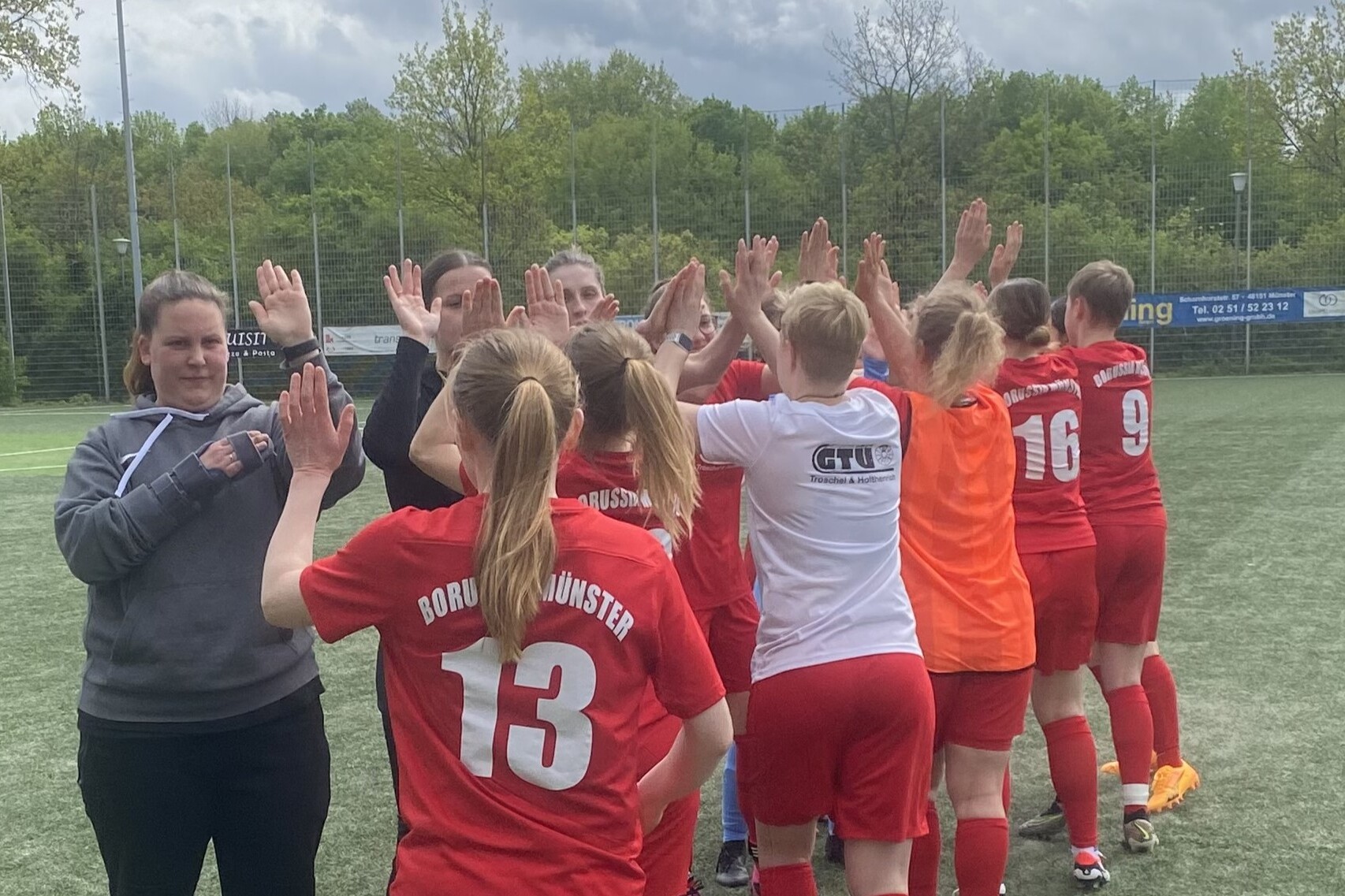 M&auml;dchenfu&szlig;ballmannschaft gibt sich in roten Trikots zur Begr&uuml;&szlig;ung High-Fives auf einem Sportplatz.