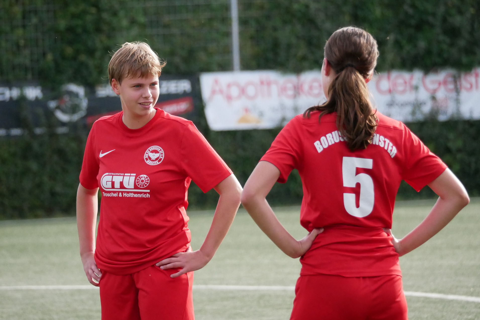 Zwei Fu&szlig;ballspielerinnen in roten Trikots stehen auf dem Spielfeld und unterhalten sich.