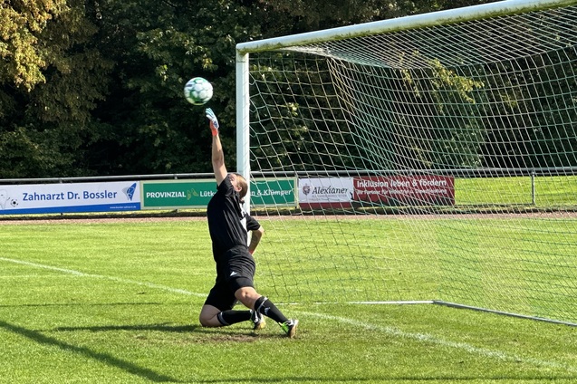 Torwart springt auf dem Fu&szlig;ballfeld, um einen Ball im h&ouml;heren Bogen zu halten, w&auml;hrend er vor dem Tor kniet.