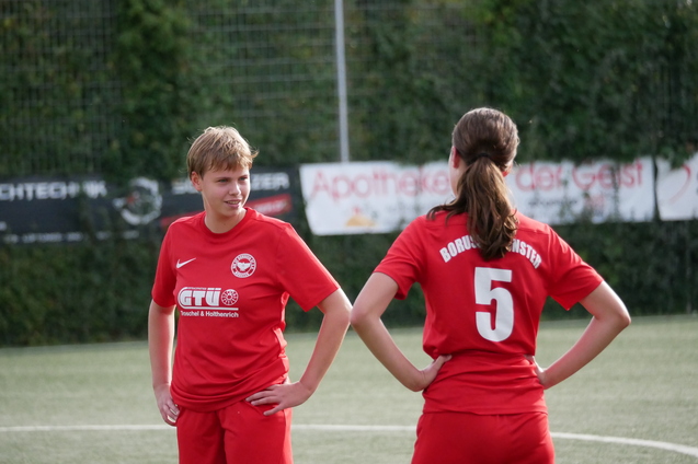 Zwei Fu&szlig;ballspielerinnen in roten Trikots stehen auf dem Spielfeld und unterhalten sich.