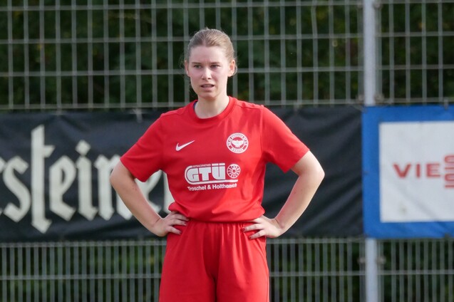 Junge Fu&szlig;ballerin in rotem Trikot steht auf dem Platz und blickt konzentriert in die Ferne.