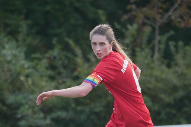 Nahaufnahme einer Fu&szlig;ballspielerin in rotem Trikot mit buntem Schwei&szlig;band, die sich auf dem Spielfeld umdreht.