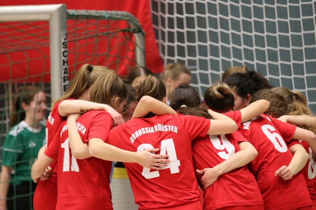 Gruppe von M&auml;dchen in roten Trikots umarmt sich vor einem Fu&szlig;balltor. Im Hintergrund ist eine Torwartspielerin zu sehen.