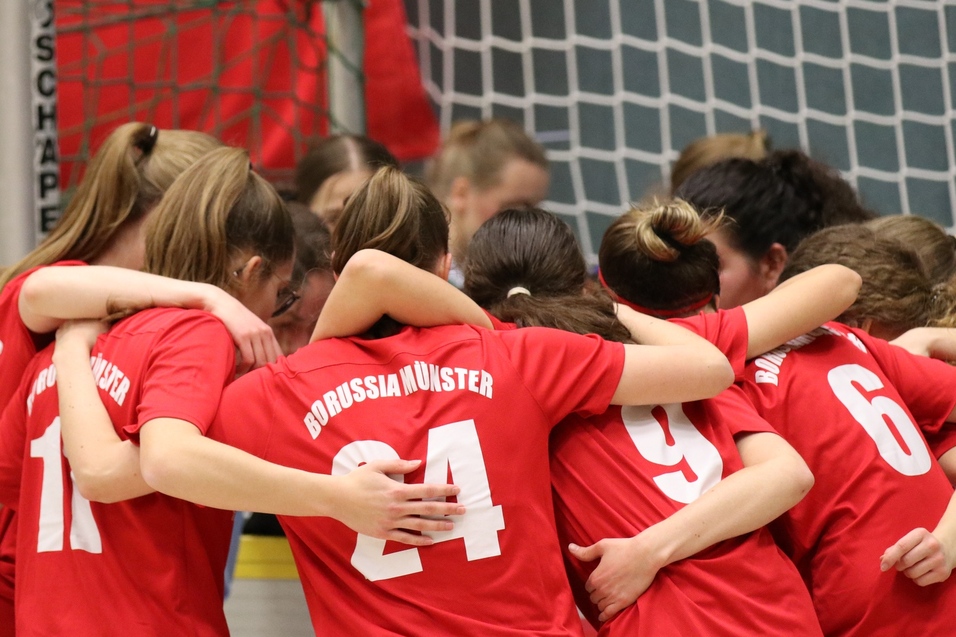 Gruppe von M&auml;dchen in roten Trikots umarmt sich vor einem Fu&szlig;balltor. Im Hintergrund ist eine Torwartspielerin zu sehen.