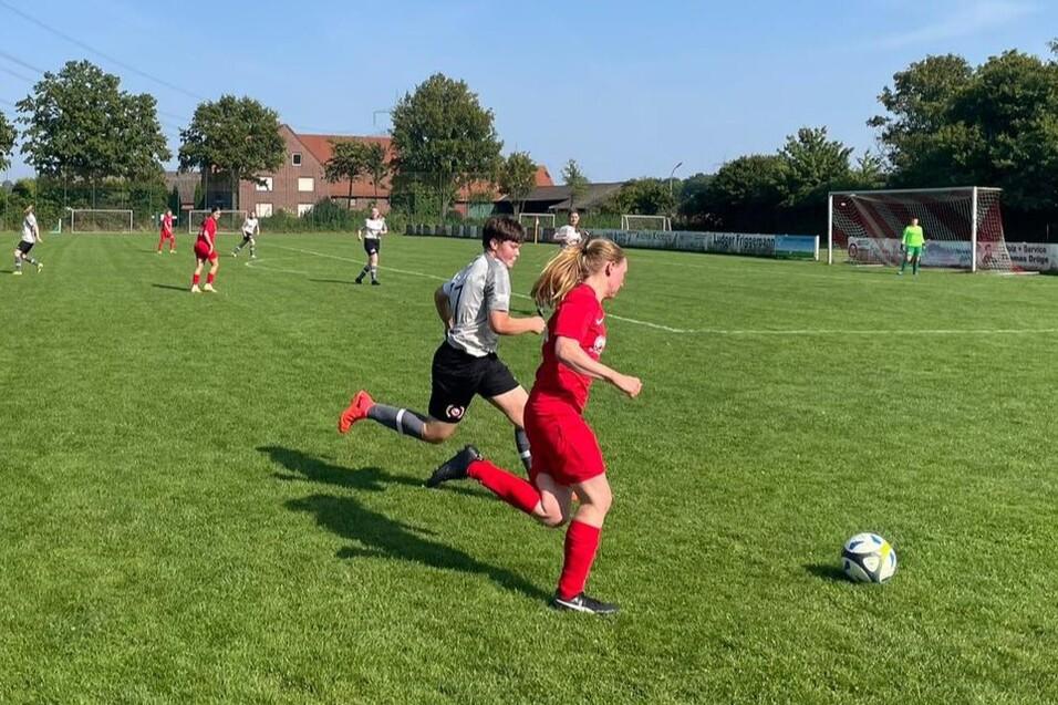 Fu&szlig;ballspiel auf einem gr&uuml;nen Platz, eine Spielerin in rotem Trikot dribbelt den Ball, w&auml;hrend ein Gegenspieler n&auml;her kommt.